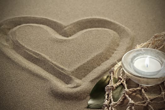 handwritten heart on yellow soft sand with lighted candles