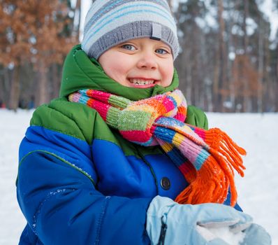 Cute boy plaing with snow in winter forest.