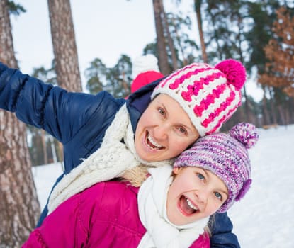Happy young mother and daughter in winter clothing to have fun in winter forest