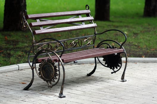 Metal forged bench in autumn park with leafs and sunflower