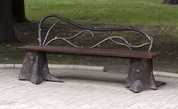 Metal forged bench in autumn park with branches and stumps