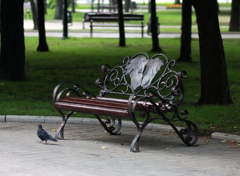 Metal forged bench in autumn park with a couple of lovers in heart