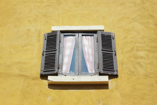 Old wooden window open on yellow wall.