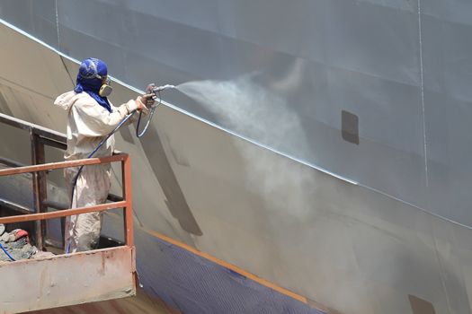 worker painting ship hull using airbrush gray paint