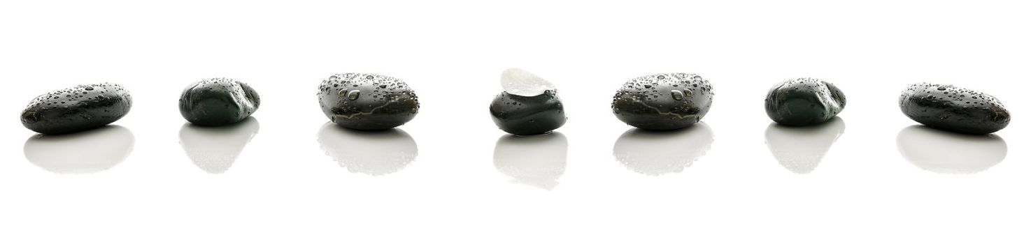 Spa stones in a row with water drops. White flower petal on top of the middle one.