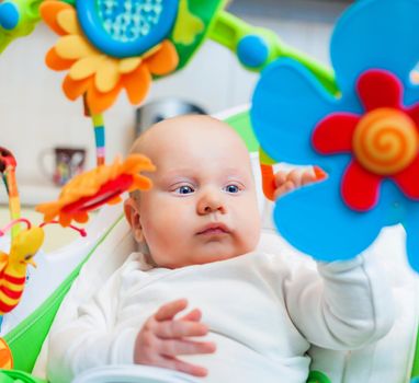 Closeup portrait of sweetest baby girl playing with a colorful mobile toy
