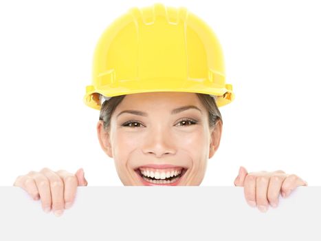 Construction worker / engineer woman showing sign wearing yellow hard hat. Happy young woman holding and peaking over white blank billboard sign card isolated on white background. Multiracial woman.