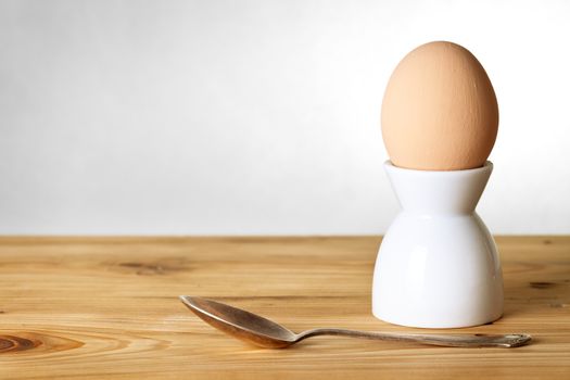 Easter composition with egg on stand and spoon on wooden background. Egg painted a beige paint 
