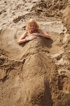 girl buried under sand is looking at you