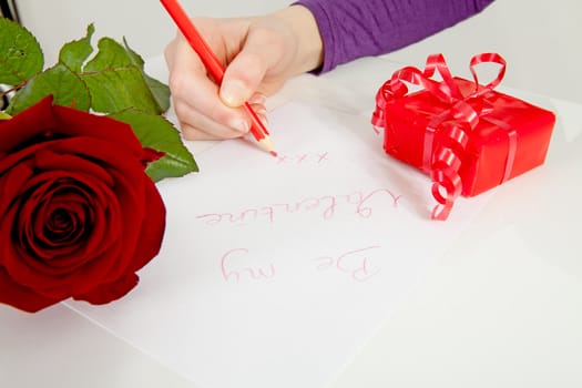 Hand is writing Be my valentine in closeup with rose and present