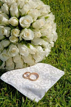 Golden wedding rings and bouquet of roses on grass