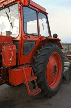 Red wheel tractor with  shovel in  parking lot on sky background.