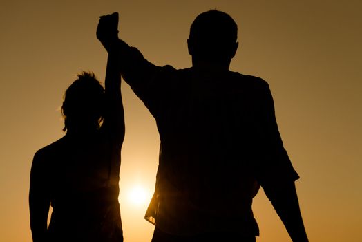 Silhouette of loving couple raise their hands together over orange sunset background