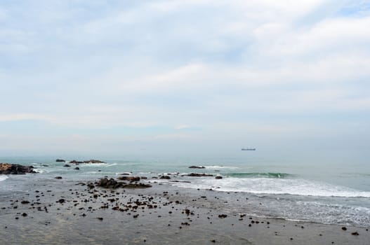  Stony shore with misty sea, cargo ships and cloudy sky