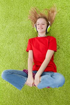 girl is listening to music with headphones on lying in green carpet