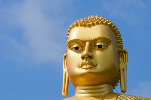 Golden yellow Buddha statue head on blue sky background