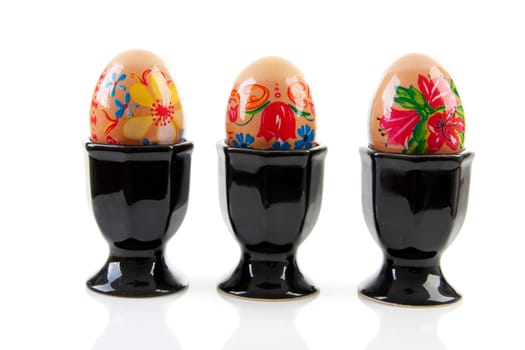 Three chicken eggs decorated by children in black holder over white background