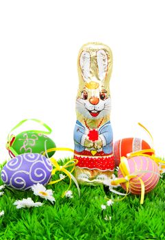 Chocolate easter bunny and colorful eggs on grass over white background
