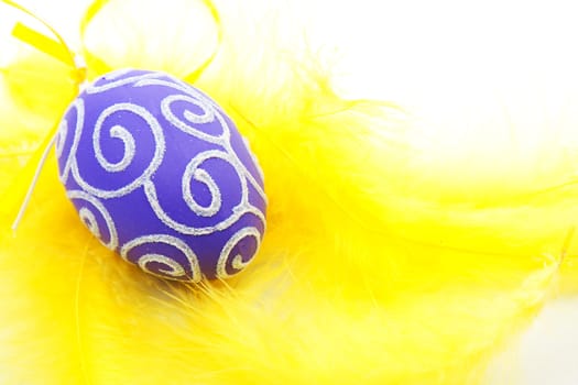 purple easter egg on yellow feathers in closeup