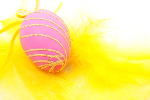 Pink easter egg on yellow feathers in closeup