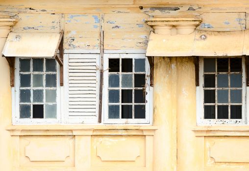 Grunge ramshackle windows with broken glass on yellow wall