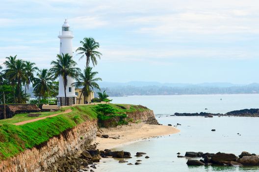 White lighthouse on fortified stone wall with cloudy sky background, Galle, Sri Lanka