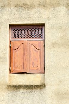 Small wooden window with close shutters on yellow wall 