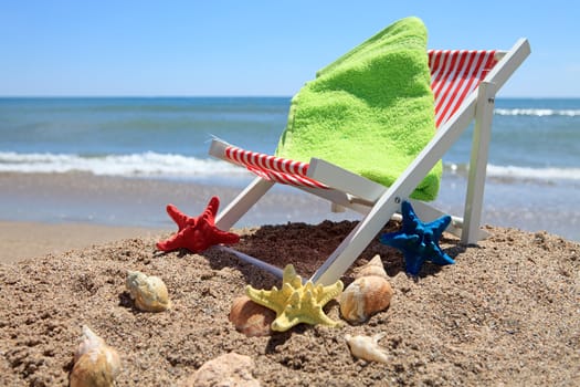 Beach chair and green towel near the ocean with shells on sunny day