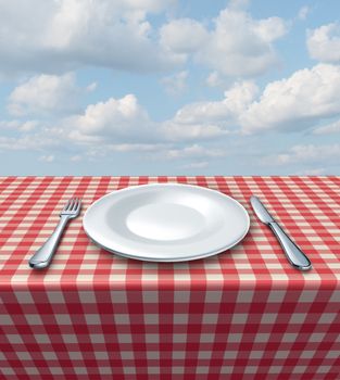 Place setting with a fork knife and white empty plate on a checkered red and white tablecloth on a summer blue sky as a food service and classic restaurant symbol and picnic dining.