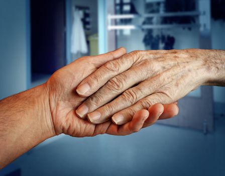Elderly care and senior health services with the hand of a young person holding and helping an old and aging retired patient needing in home medical help due to aging and memory loss in a hospital background.