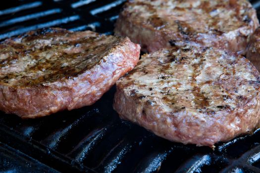 Beef quarterpounder burgers begin to cook on the gas barbecue