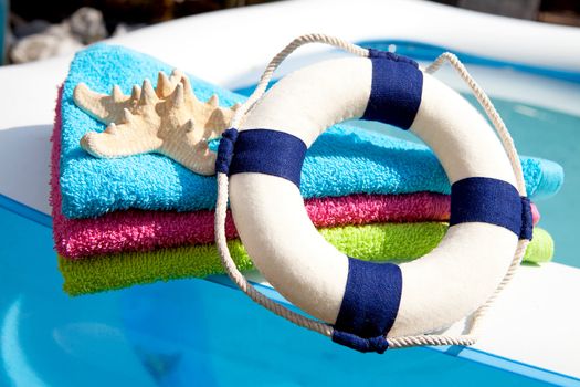 summer gear; colorful towel, life buoy and starfish by the swimpool