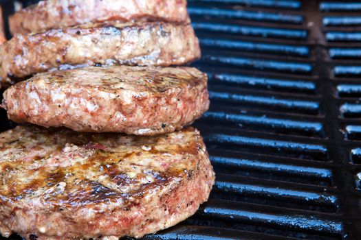 Beef quarterpounder burgers begin to cook on the gas barbecue