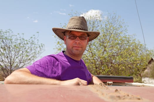 Going on safari: man standing on top of jeep with hat on