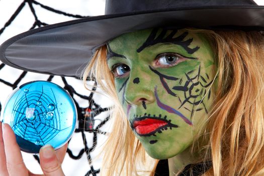 Portrait of green Halloween witch girl holding big blue marble in closeup