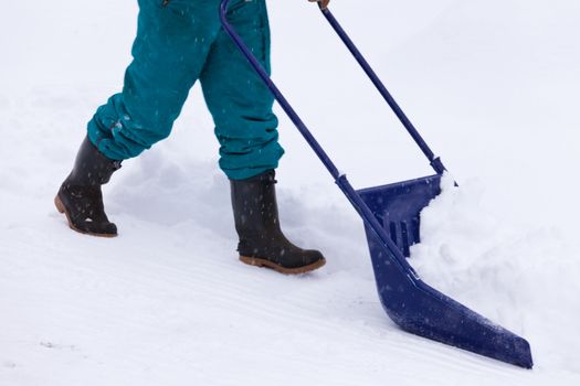 Manual snow removal from driveway using a snow scoop by person wearing boots
