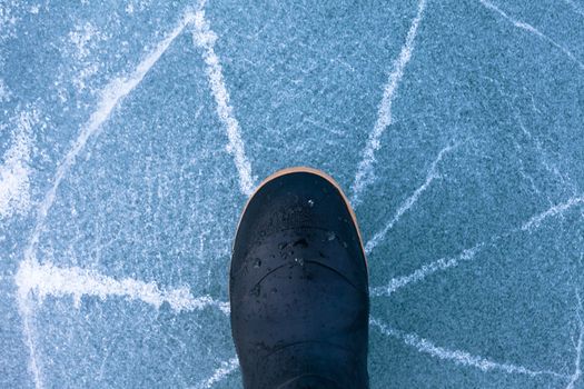 Thin ice cracking under weight of rubber boot human foot walking with cracks radiating outwards signalling high danger