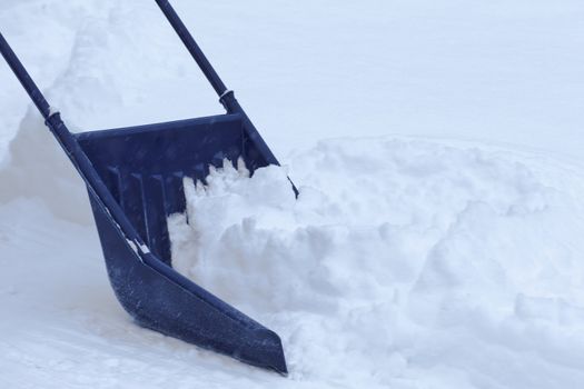 Manual snow removal from driveway using a snow scoop after blizzard