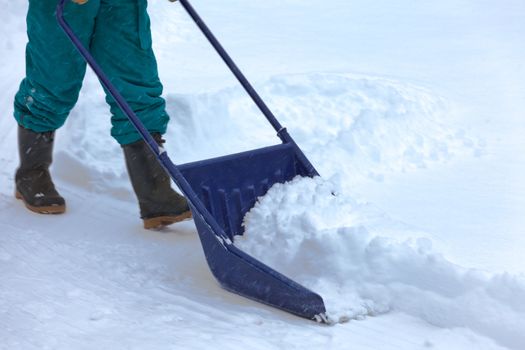Manual snow removal from driveway using a snow scoop by person wearing boots