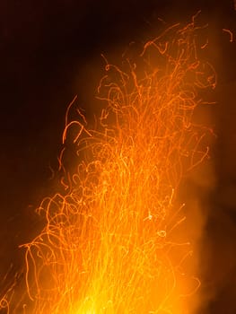 Hot orange spark trails bursting up from hell fire such as big bonfire steel making or welding