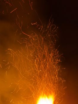Hot orange spark trails bursting up from hell fire such as big bonfire steel making or welding