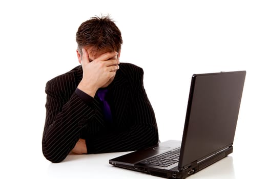 Businessman sitting behind desk is in despair, covering his eyes, over white background