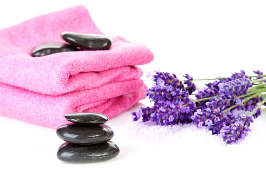 Spa accessories: stacked black pebbles stones, pink towels and lavender flowers over white background