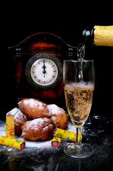 Dutch donut also known as oliebollen, traditional New Year's eve food and clock on midnight, firework, champagne over black background