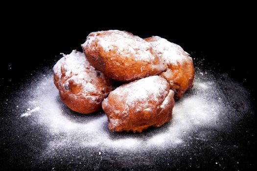 pile of Dutch donut also known as oliebollen with powdered sugar, traditional New Year's eve food isolated on black background 

