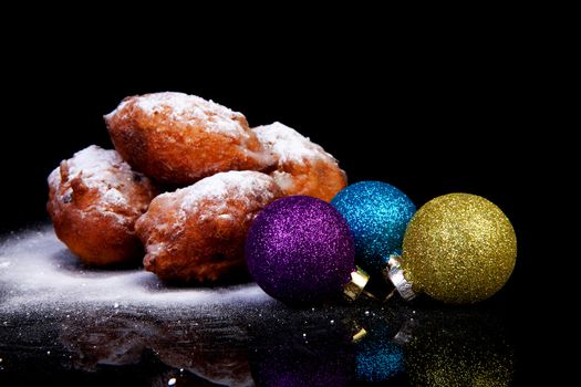 Pile of Dutch oliebollen and Christmas balls over black background