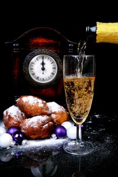 Pouring champagne on New Year's Eve with Dutch olibollen over black background
