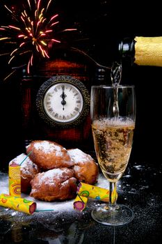 Dutch donut also known as oliebollen, traditional New Year's eve food and clock on midnight, firework, champagne over black background