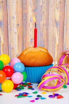 Birthday cupcake with candle and colorful confetti over wooden background