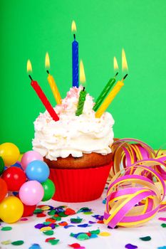 Birthday cupcake with lots of candles, party streamers and colorful confetti over green background